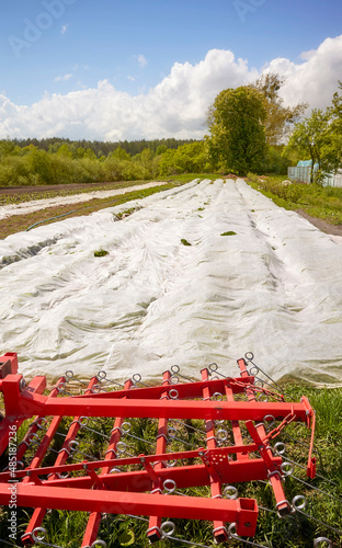 Eco farm with agriculture equipment and nonwoven agrotextile covering field, focus on the foreground.