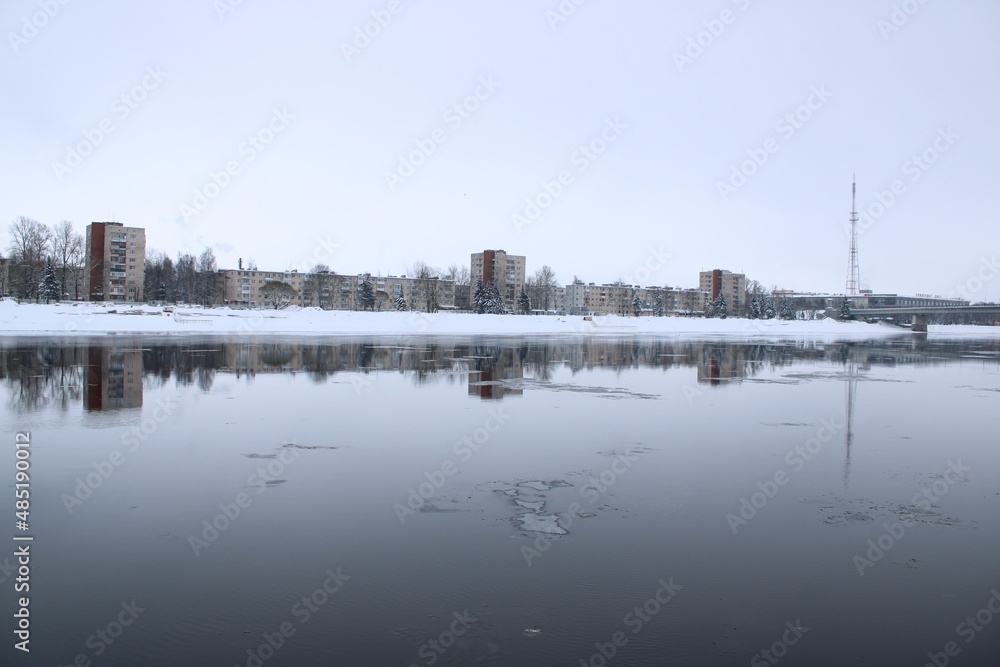 winter in the city, view on the river, snowy coast and stone houses and tower reflected in water