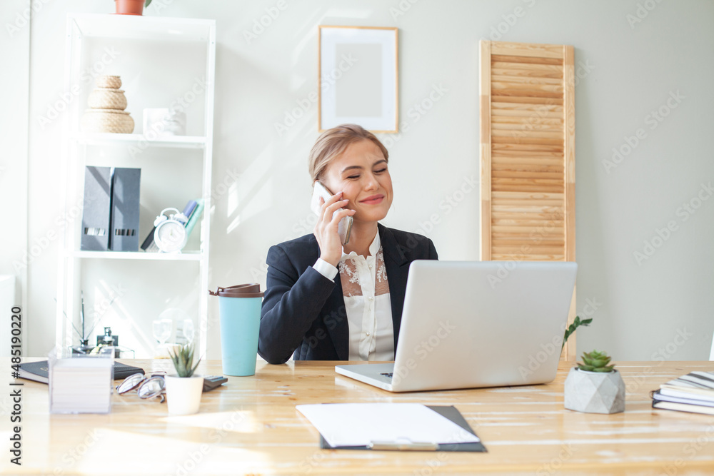 Portrait of executive financial woman sitting at desk and working on laptop while making call Portrait of executive financial woman sitting at desk and working on laptop while making call