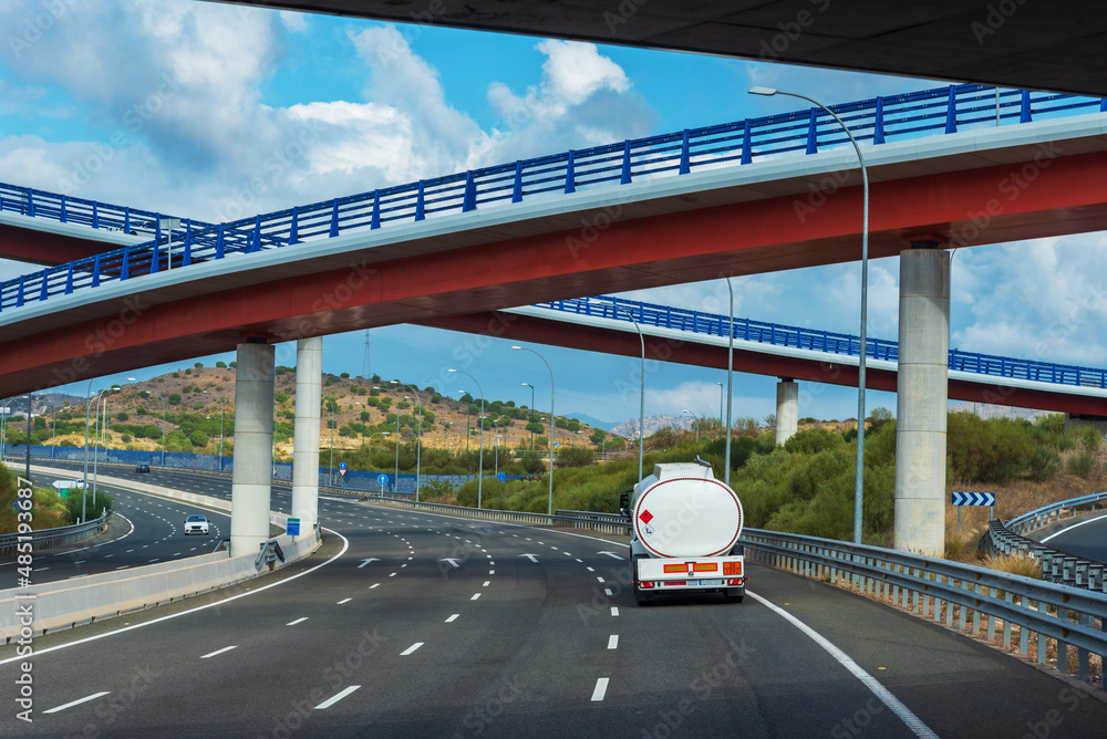 Dangerous goods tanker truck driving under some highway bridges.