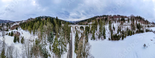 Wiadukt kolejowy w górach zimą nad rzeką i drogą. Wisła, Beskid Śląski w Polsce