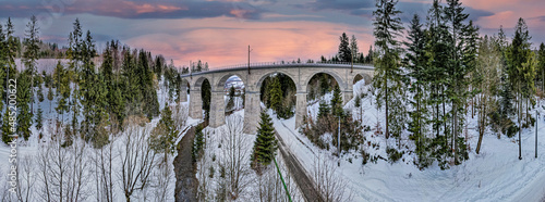 Wiadukt kolejowy w górach zimą nad rzeką i drogą. Wisła, Beskid Śląski w Polsce