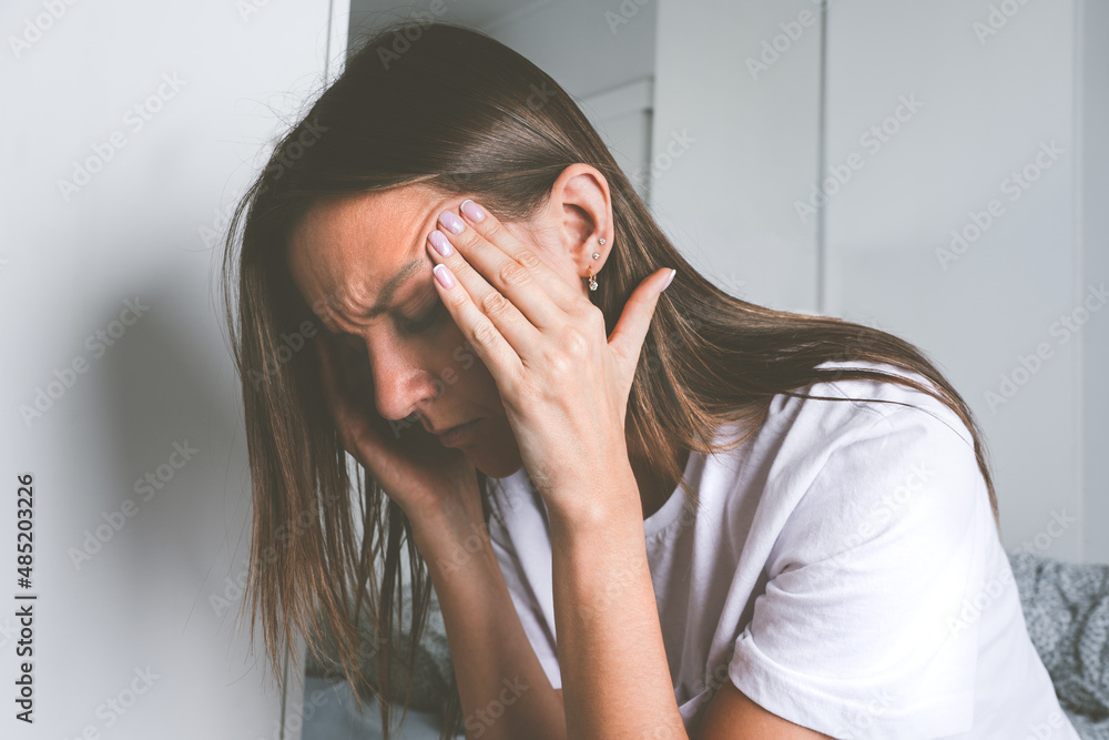 Young woman touching her temples and suffering from head pain, headache or migraine after waking up Young woman touching her temples and suffering from head pain, headache or migraine after waking up