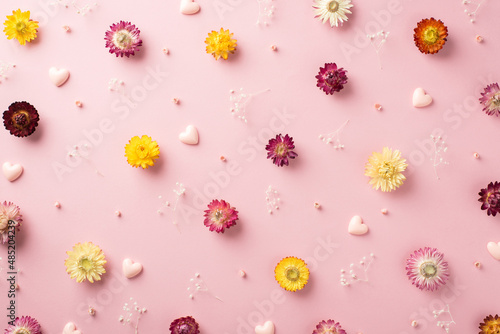 Top view photo of the many different colorful flowers with branches of gypsophila and pink volume confetti in shape of hearts scattered on the pastel pink background