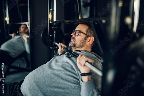 Middle aged man lifting barbell while training in the gym