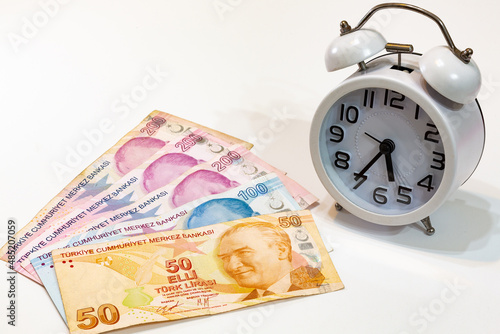 50, 100 and 200 Turkish banknotes and alarm clock on isolated white background. Time is money concept.
