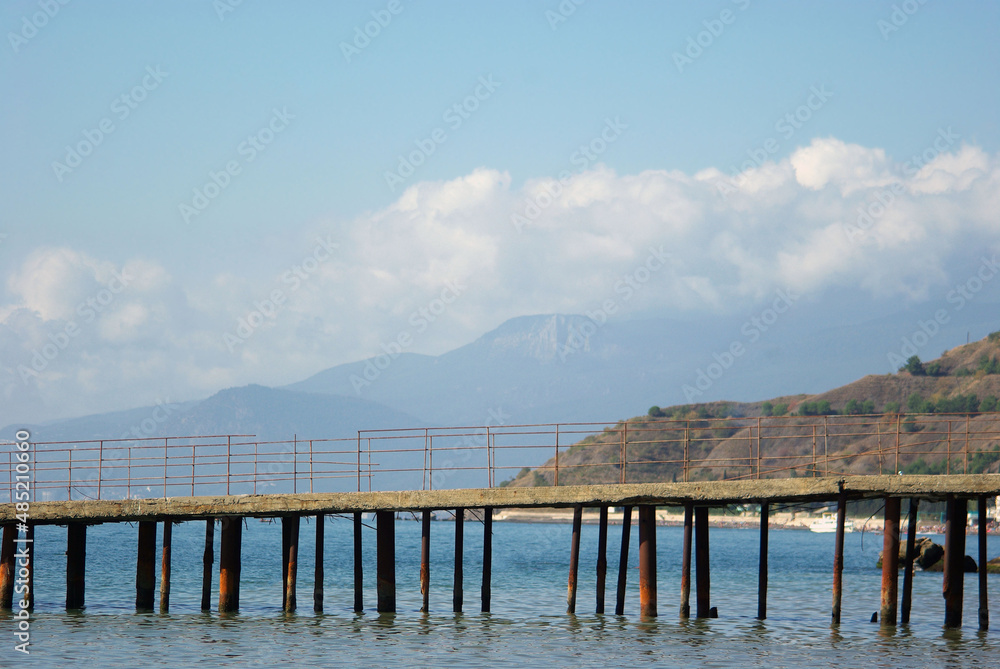 Old pier in Crimea with mountains and clouds at background