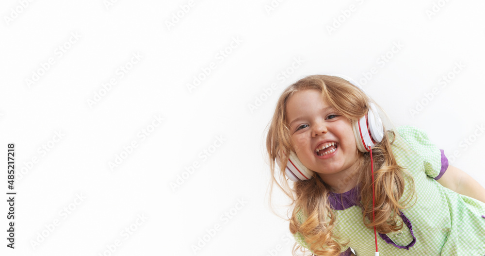 Cheerful funny little girl in headphones on white background. Music or entertainment online. Banner with copy space Cheerful funny little girl in headphones on white background. Music or entertainment online. Banner with copy space