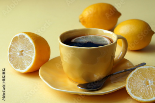 yellow cup of tea with lemon and yellow fruits of lemons on a yellow background