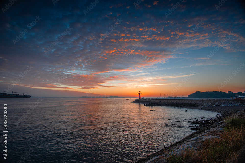 A harbor in the dawn sky with a lighthouse visible
