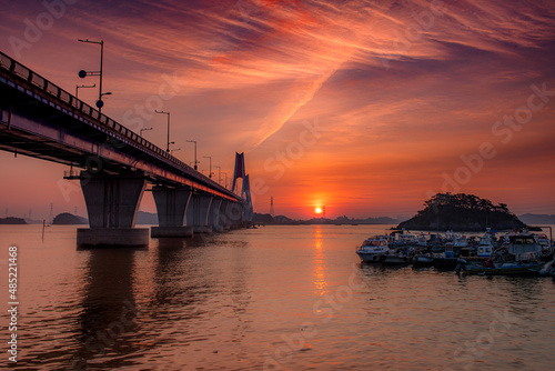 A bridge across the sea and a small fishing boat floating on the sea and the dawn sky  © Kim Sehwan
