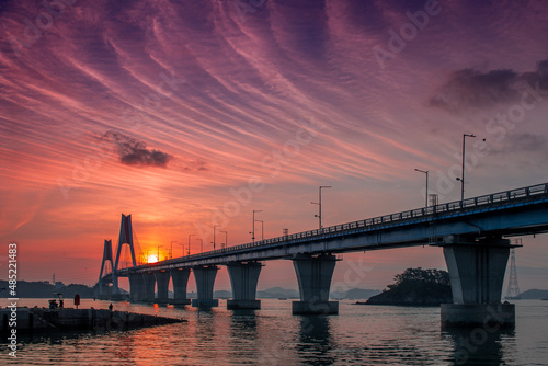 A bridge across the sea and a small fishing boat floating on the sea and the dawn sky
