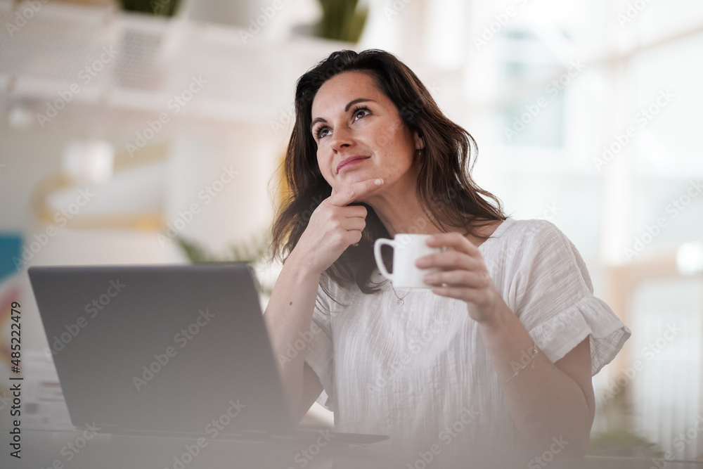 happy smiling remote working woman drinking coffee or espresso infront of a laptop or notebook on her work desk in her modern airy bright living room home office happy smiling remote working woman drinking coffee or espresso infront of a laptop or notebook on her work desk in her modern airy bright living room home office