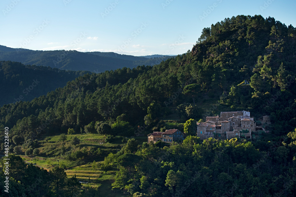 Village typique cévenole au pied d'une montagne avec ses cultures en terrasse. Vallée sauvage boisée. France.