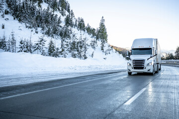 Bonnet big rig white semi truck transporting cargo in dry van semi trailer running on the winter dangerous slippery road with snow and ice in Montana