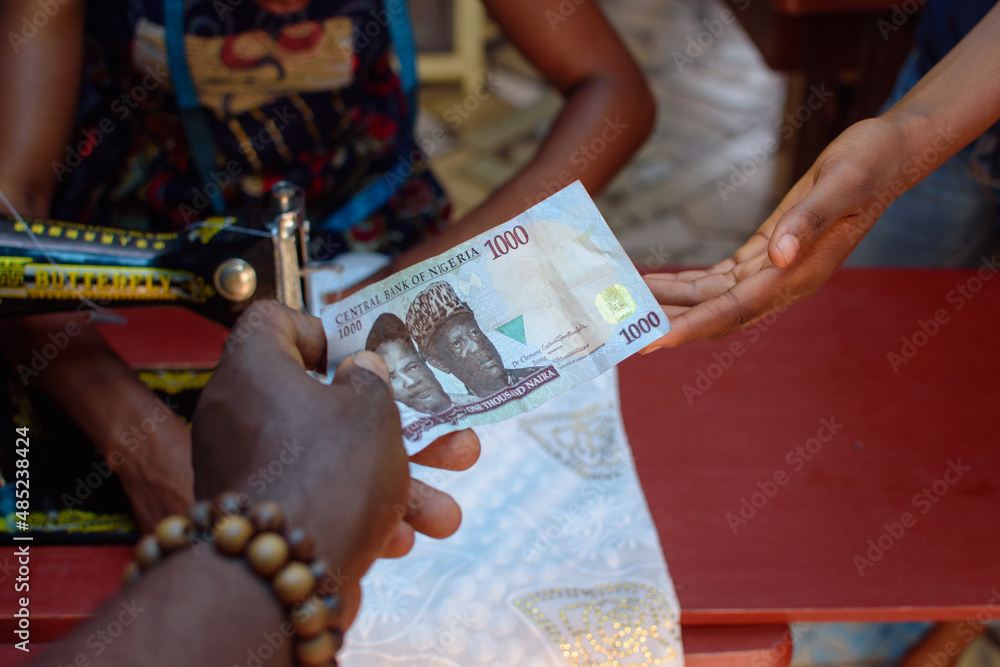 African hands exchanging cash, money or the Nigerian currency know as Naira in a tailoring shop for business purpose and with a sewing machine in the background
