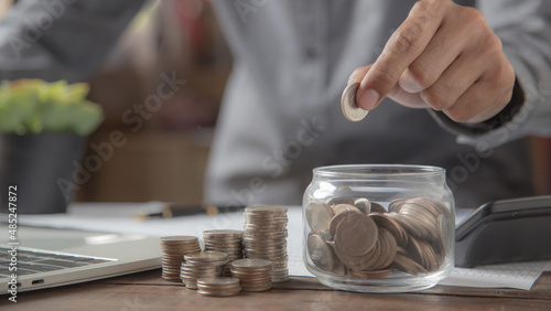 Businessman put a coin in a cup with pile of coins stacked in a graph for money saving planning ideas.