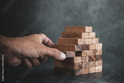Hand pull wooden block stack in pyramid stair step concept of prevent collapse or crash of financial business and risk management or strategic planning and insurance.