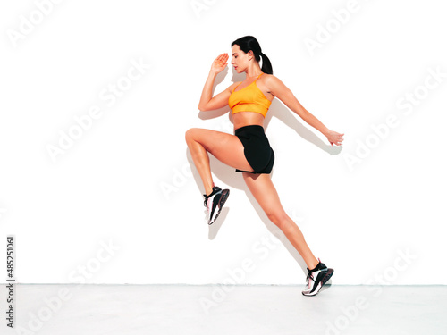 Fitness woman in sexy sports clothing. Young beautiful model with perfect body. Female posing in studio near white wall at summer sunny day. Jumping and running