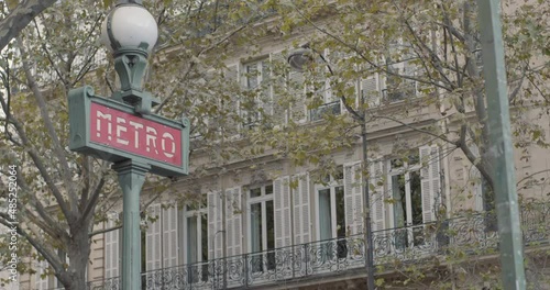 Dolly push in pull back shot of art deco metro sign in Paris with trees, apartments in background photo
