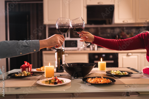 romantic dinner for two, couple with glasses of red wine in home kitchen, hands close up, date clink glasses, birthday or anniversary at home, alcohol