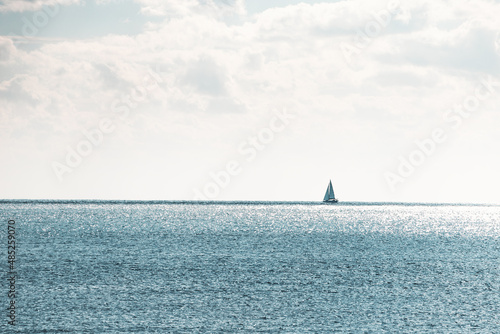Minimalistic landscape with a lone sail in the boundless blue sea