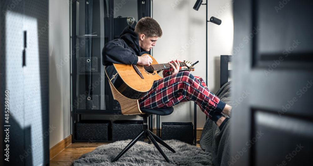 A young man plays the acoustic guitar in his room at home. A young man plays the acoustic guitar in his room at home.