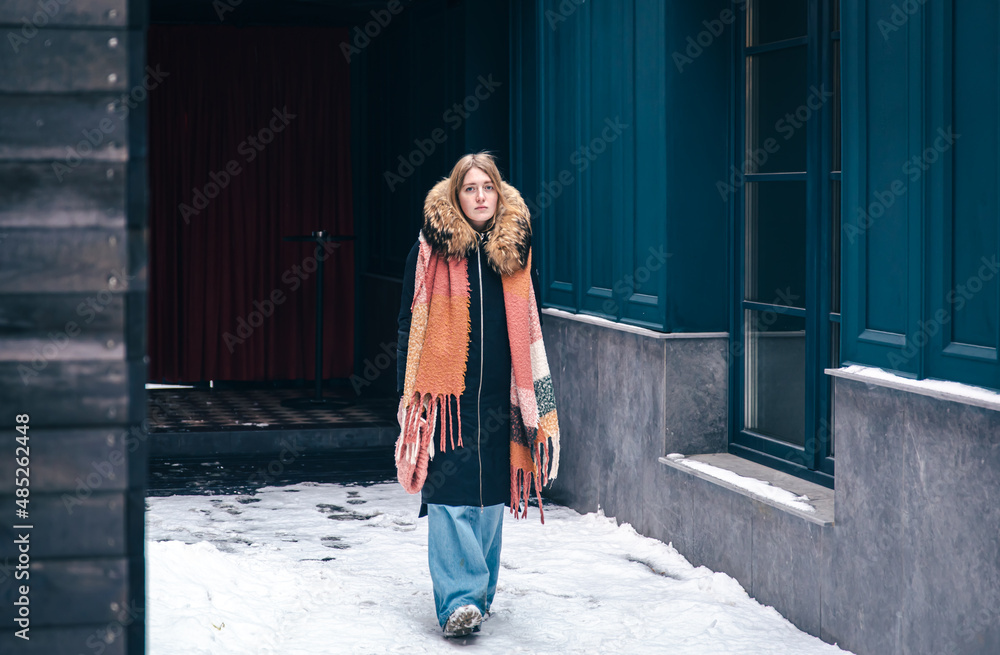 Stylish young woman in a jacket and with a scarf on a walk in winter.