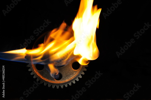 Gear wheel in flame on black background.