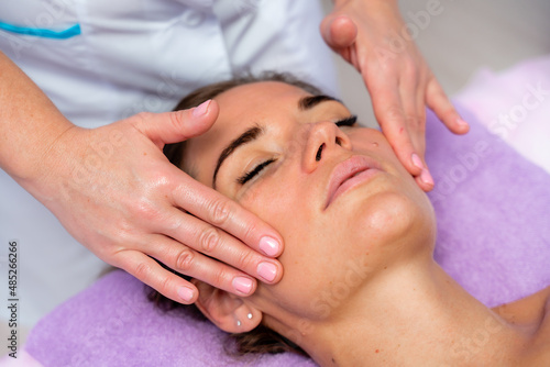 Relaxing massage. European woman getting facial massage in spa salon  side view