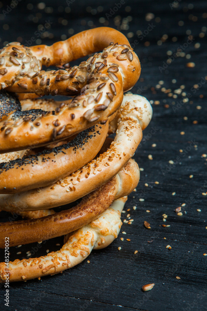 Fresh prepared homemade soft pretzels. Different types of baked bagels with seeds on a black background.