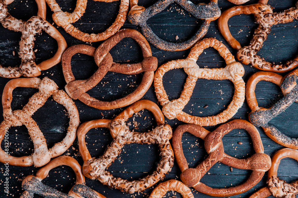 Fresh prepared homemade soft pretzels. Different types of baked bagels with seeds on a black background.