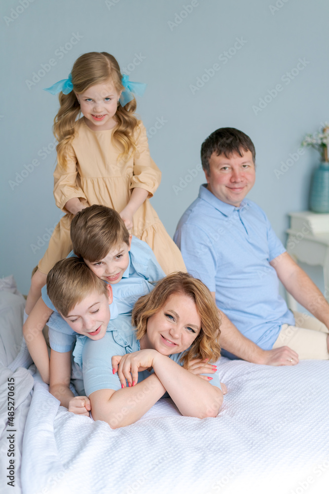 Cheerful family playing together on bed. Parents spend their free time with their daughter and two sons. Large caucasian family playing at home in bedroom. Mom and dad are fooling around with the kids
