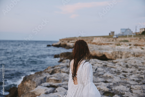 Woman in white dress walks on the beach stones back view