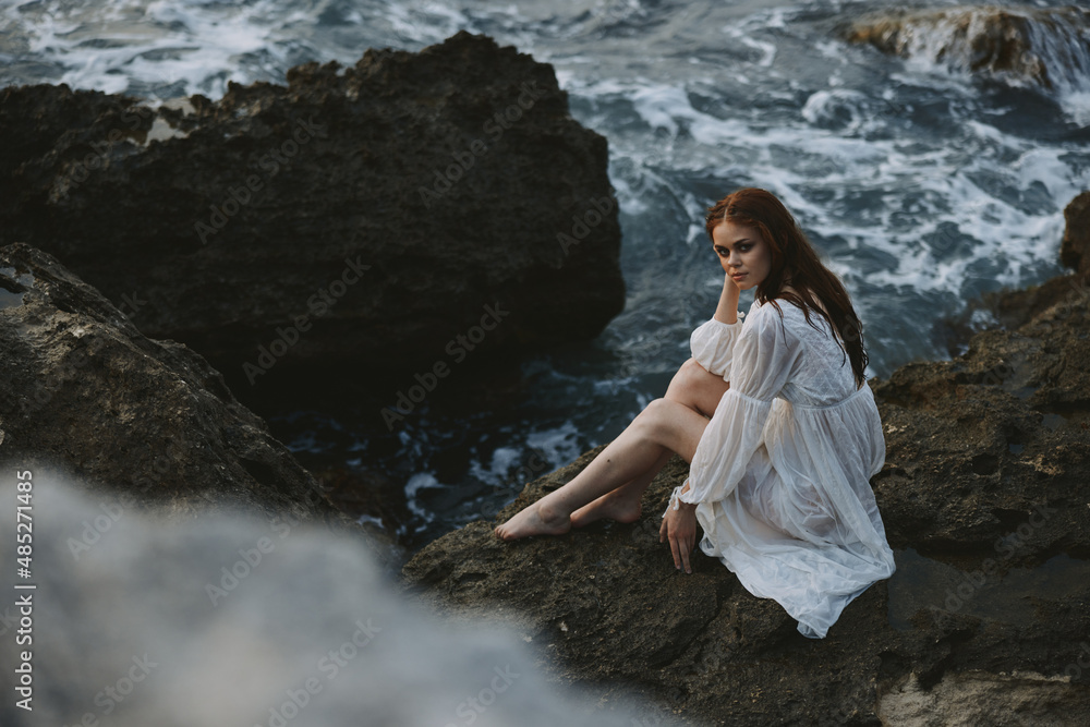 A woman in a white wedding dress is sitting barefoot on a wave cliff