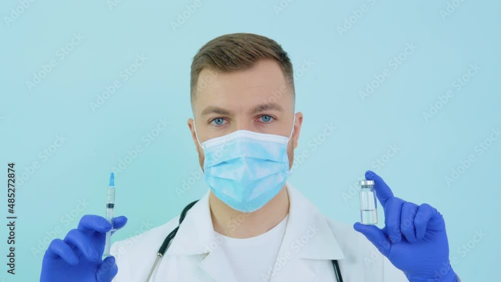 Doctor holds an ampoule with a vaccine and a syringe in his hands on a blue background Doctor holds an ampoule with a vaccine and a syringe in his hands on a blue background