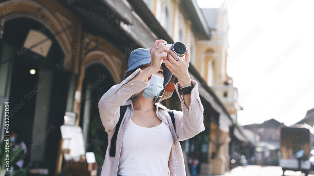 Fototapeta premium Young adult asian woman backpack traveller wear face mask take a photo by camera.