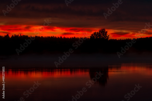 Colorful red sunset over water and lonely tree