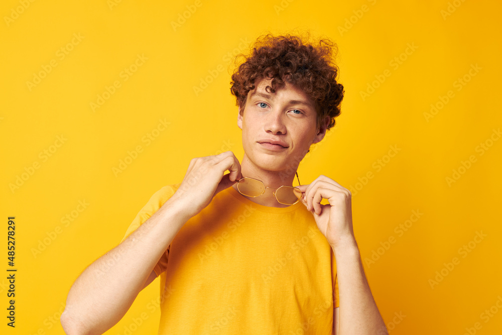 Young curly-haired man yellow t-shirt glasses fashion hand gestures yellow background unaltered Young curly-haired man yellow t-shirt glasses fashion hand gestures yellow background unaltered