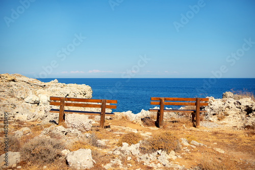 Two wooden benches on rocky seashore in Greece Rhodes Kalithea