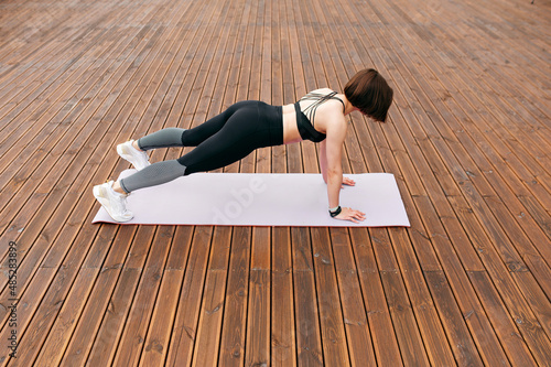 Caucasian woman standing in plank position on yoga mat and doing exercises for abs