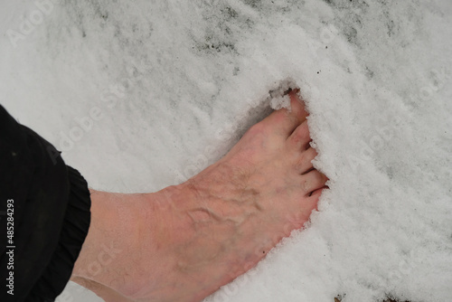 Senior walks barefoot on the snow. Bare sinewy male legs. Tempering exercises.