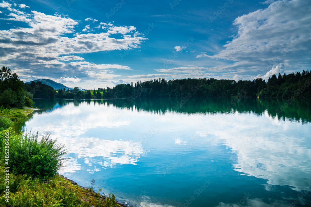 Germany, Lake water surface reflecting forest trees, clouds and sky on sunny in in bavarian nature landscape of allgaeu