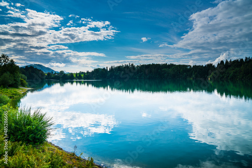 Germany, Lake water surface reflecting forest trees, clouds and sky on sunny in in bavarian nature landscape of allgaeu