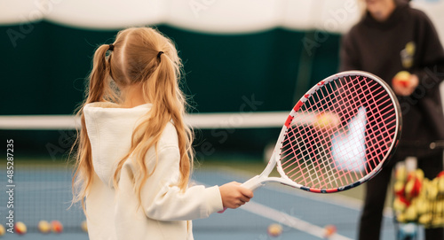 Coach teaching girl to play tennis. Child learning to hold tennis racket.