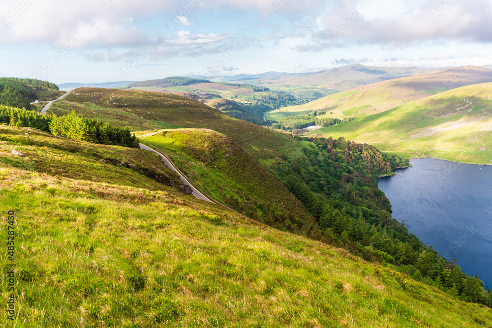 Obraz premium Landscape of a lake surrounded by the green mountains. Lough Tay scenery in Wicklow Mountains, Ireland.