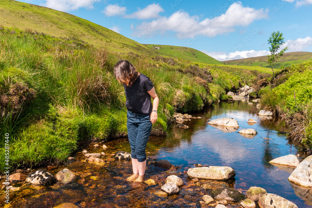 Woman hiker standing barefoot in a cold mountain stream, in Wicklow Mountains, Ireland.
Cooling off after hiking on a hot summer day.