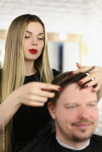 Stylish woman hairdresser combing hair to a man