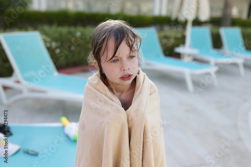Fotografi Little wet frozen child in a towel by the pool, blurry
