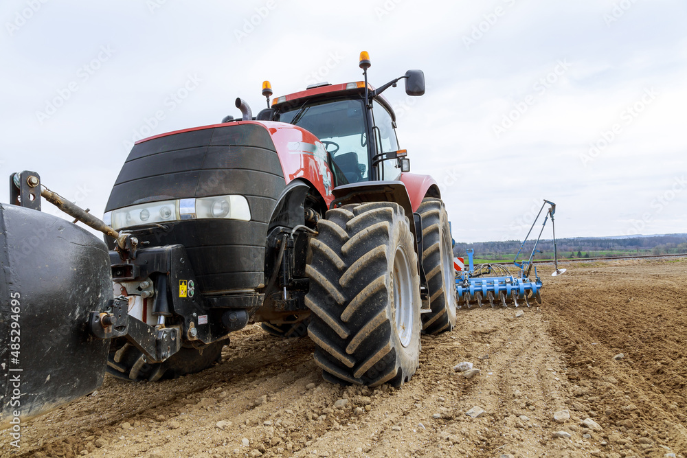Obraz premium A large red tractor close-up with sowing equipment stands in a field.